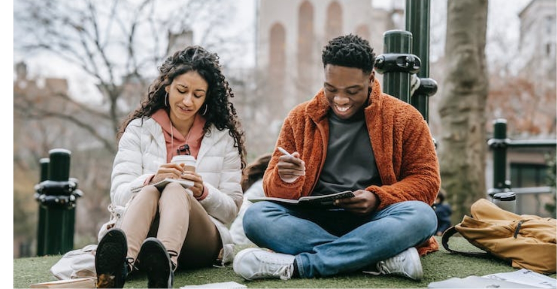 interpretive research institute Two scholars of color sitting on a grassy area in a park.